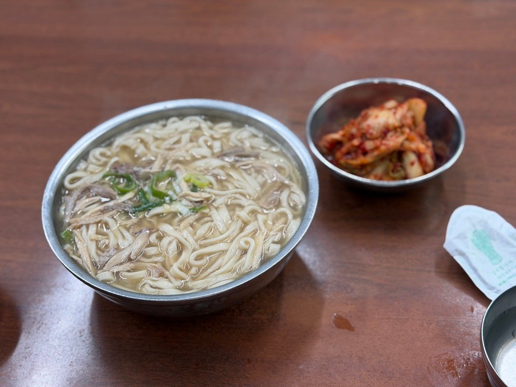 Bowl of chicken kalguksu with shredded chicken and scallions