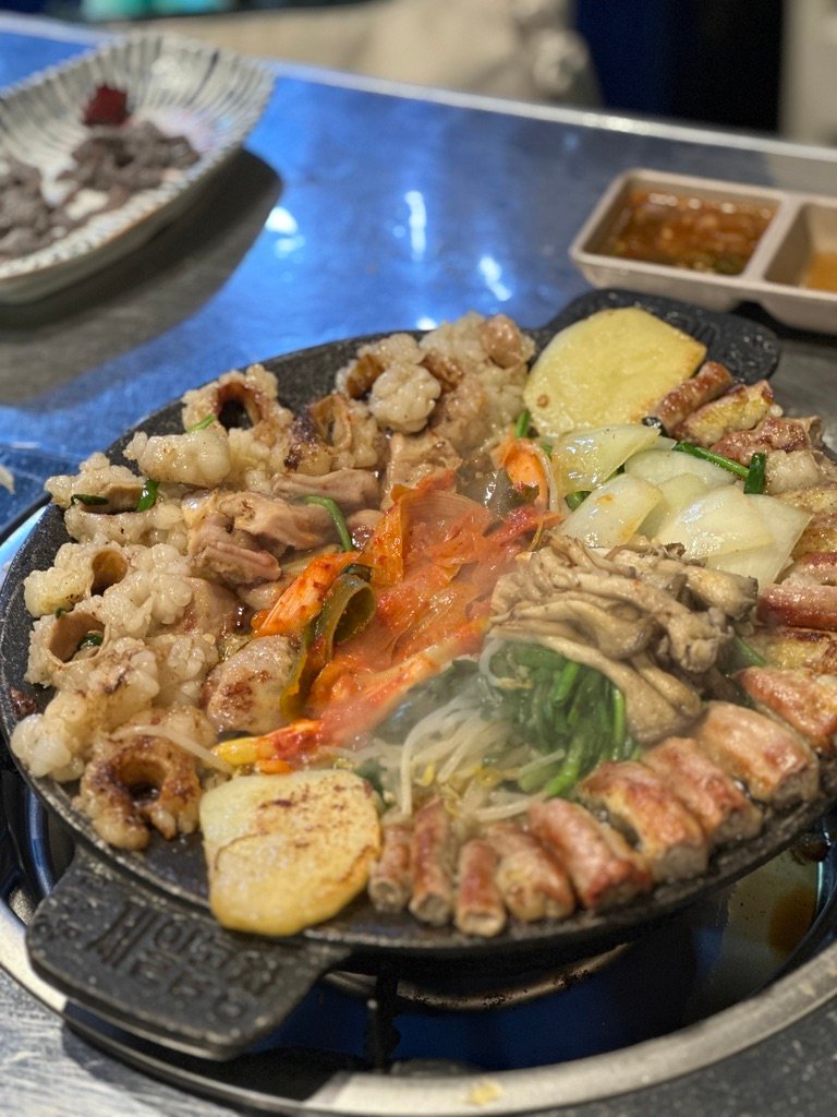 Kimchi grilling alongside beef gopchang on a table griddle