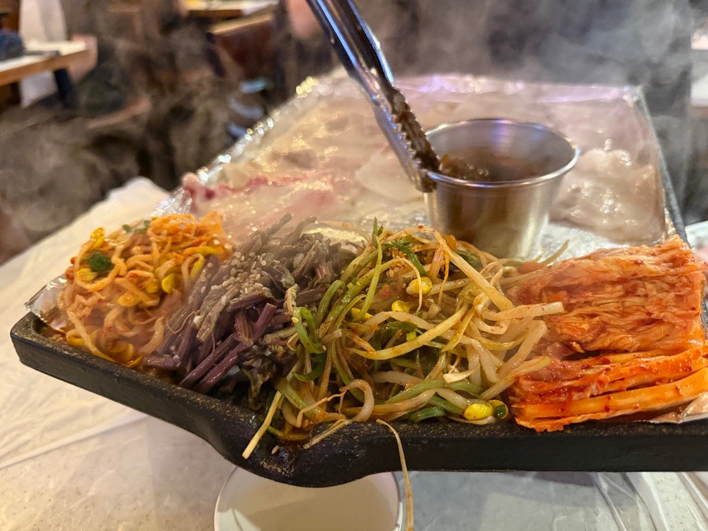 Kimchi and vegetables grilling alongside samgyeopsal on a Korean BBQ griddle