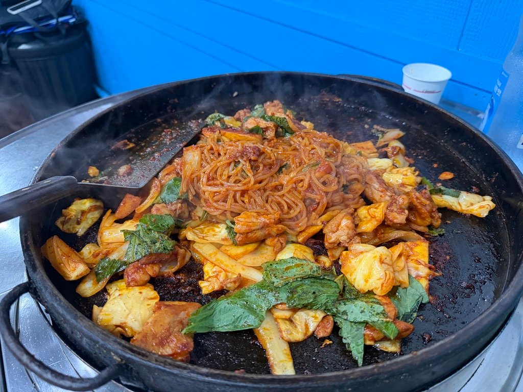 Finished dakgalbi with rice cakes and perilla leaves on a griddle