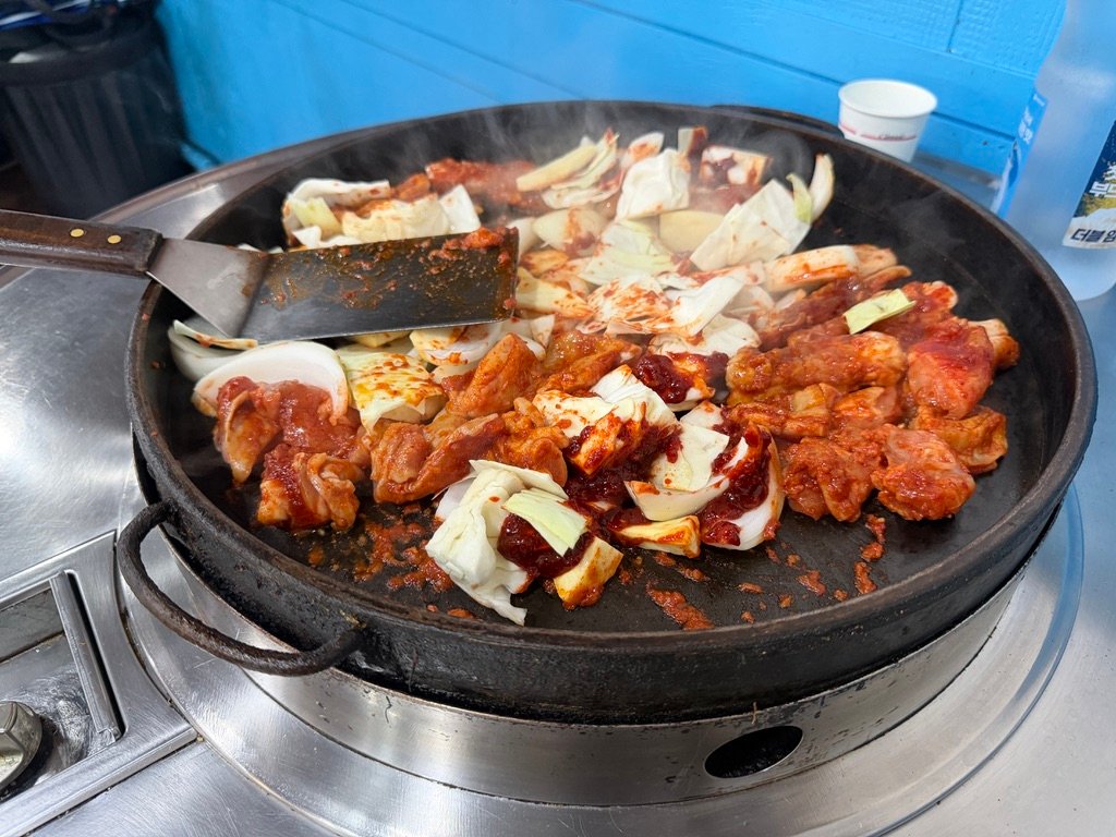 Onions added to chicken on a sizzling dakgalbi griddle
