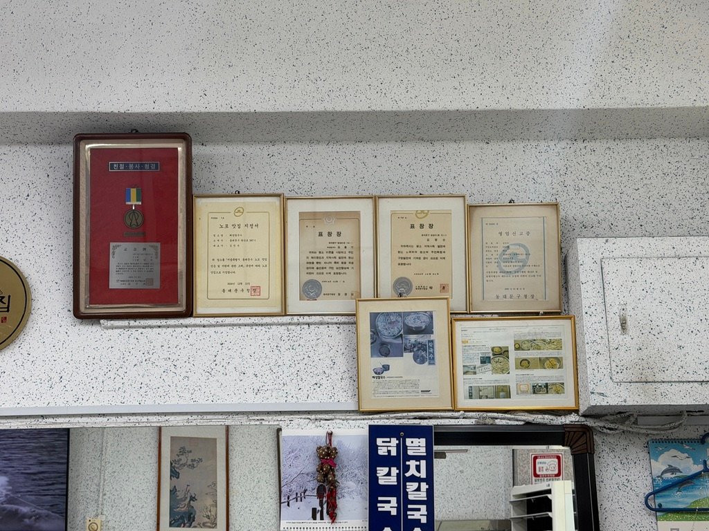 Wall display of certificates and newspaper clippings at Hyeseong Kalguksu