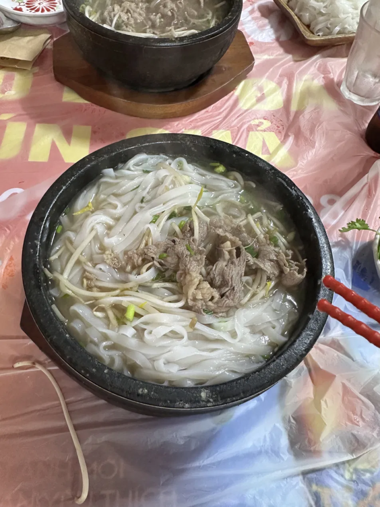 Vegetables being added to stone bowl pho at the table