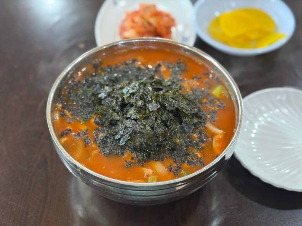 Bowl of spicy red jang-kalguksu topped with seaweed flakes and sesame seeds
