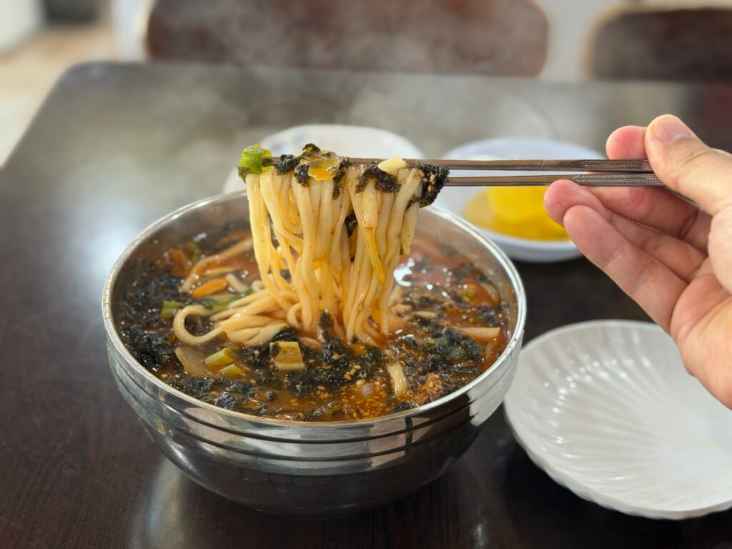 Close-up of handmade kalguksu noodles lifted with chopsticks