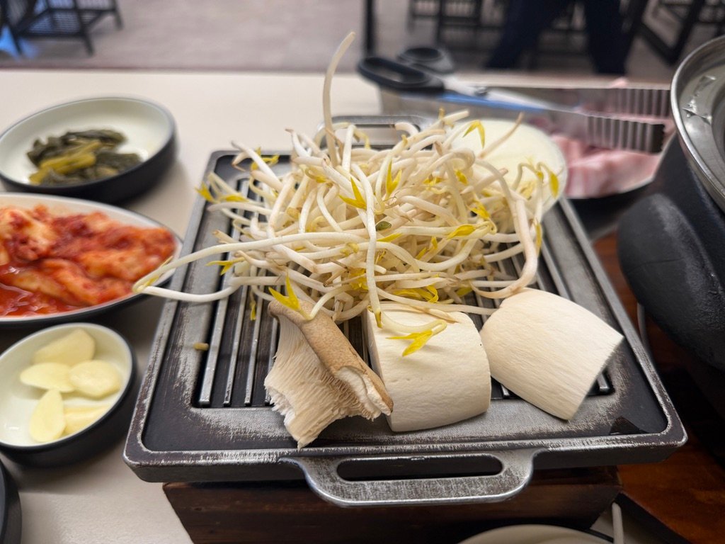 Bean sprouts and king oyster mushrooms grilling on a small brazier