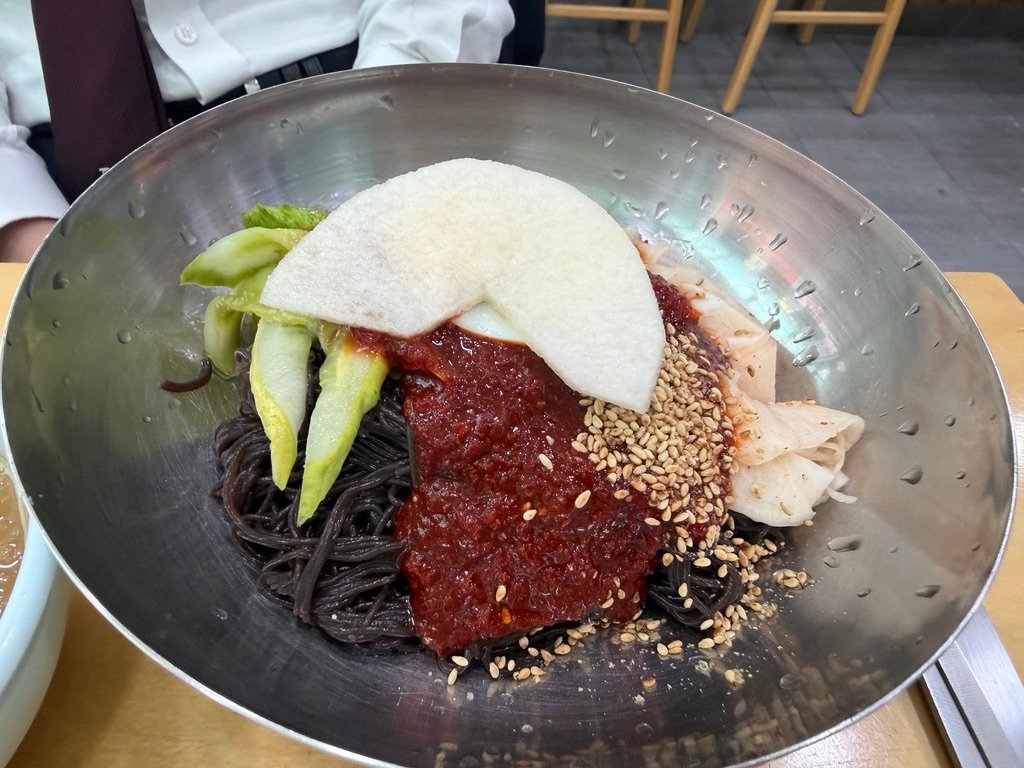 Bowl of bibim-naengmyeon topped with gochujang sauce, egg, and pear slices