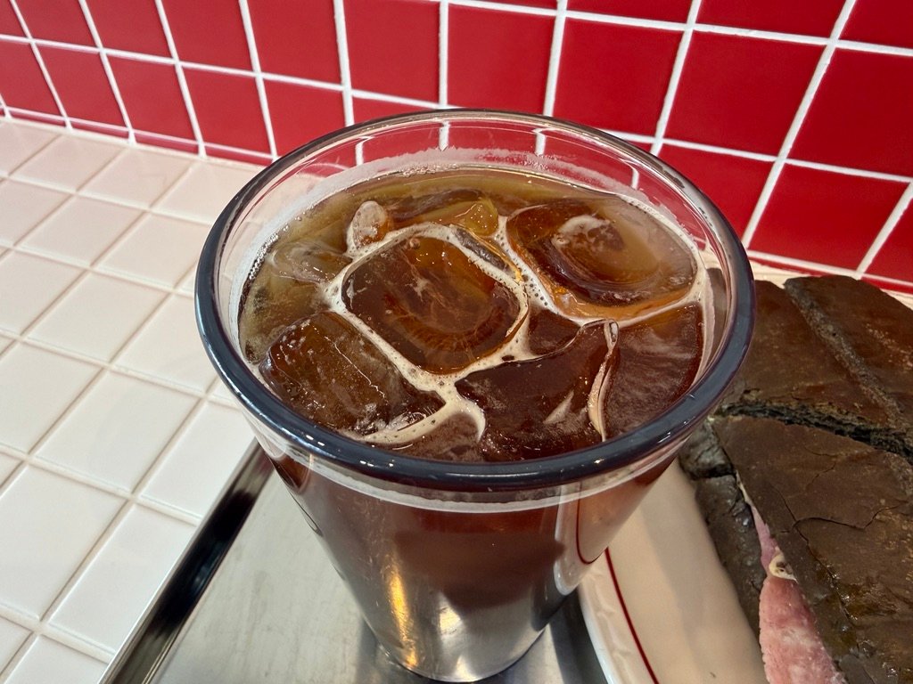 Iced Americano served alongside a sandwich at US Sandwich