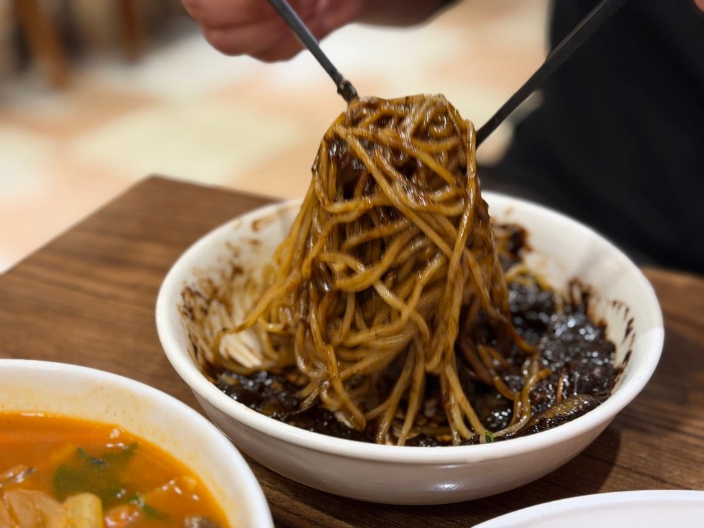 Uni-jjajangmyeon black bean noodles being lifted with chopsticks at Sillagwon